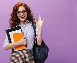 Red haired lady in eyeglasses holds books and shows ok sign. Ginger school girl with curly hair in lilac shirt and plaid skirt smiling..